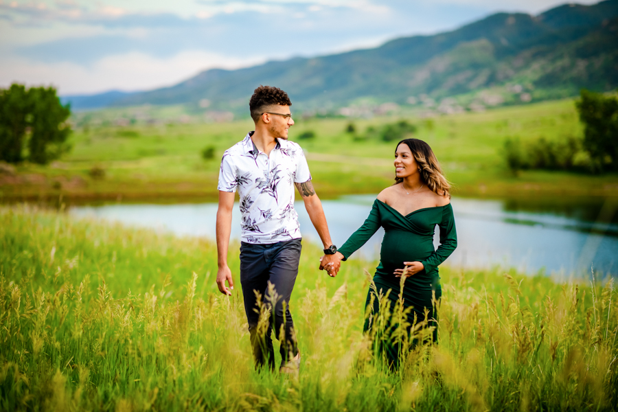 A couple walking at sunset with the Colorado foothills and a pond in the background