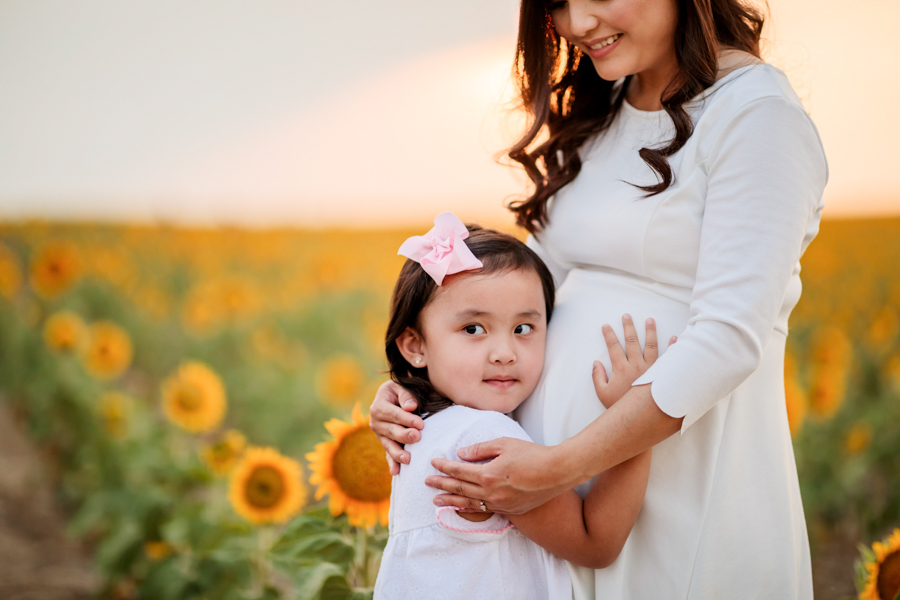 A close up shot of a baby girl listening to her mom's belly in sunflower fields at sunset in Denver