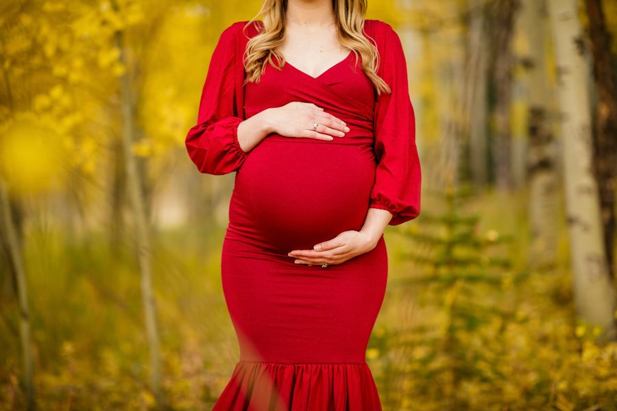 A close up shot of a woman holding her belly in a fitting red maternity dress