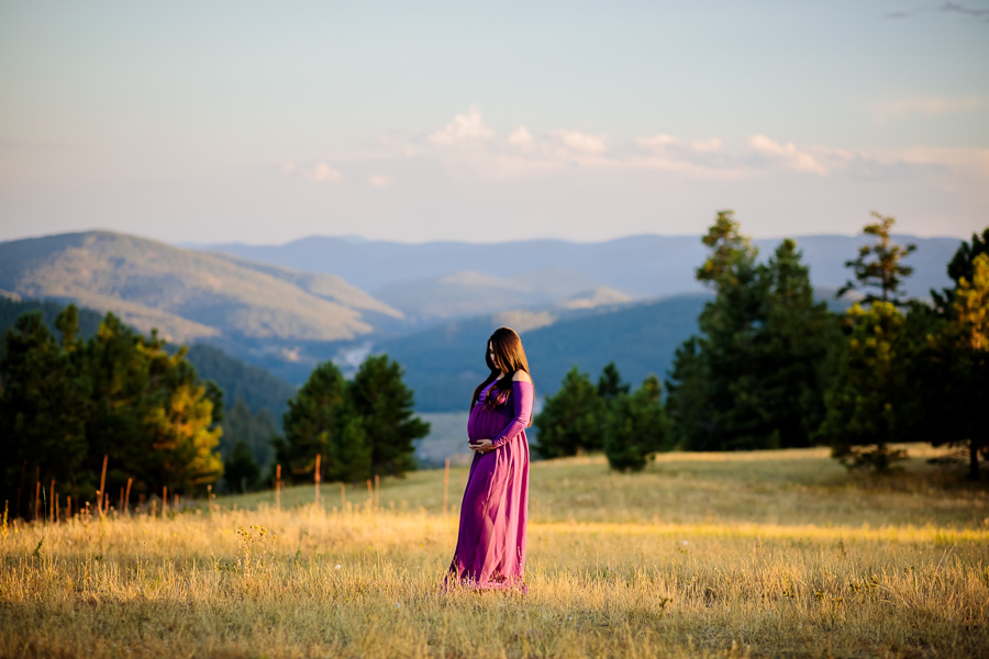 A woman in a flowy purple maternity dress posing on a mountaintop