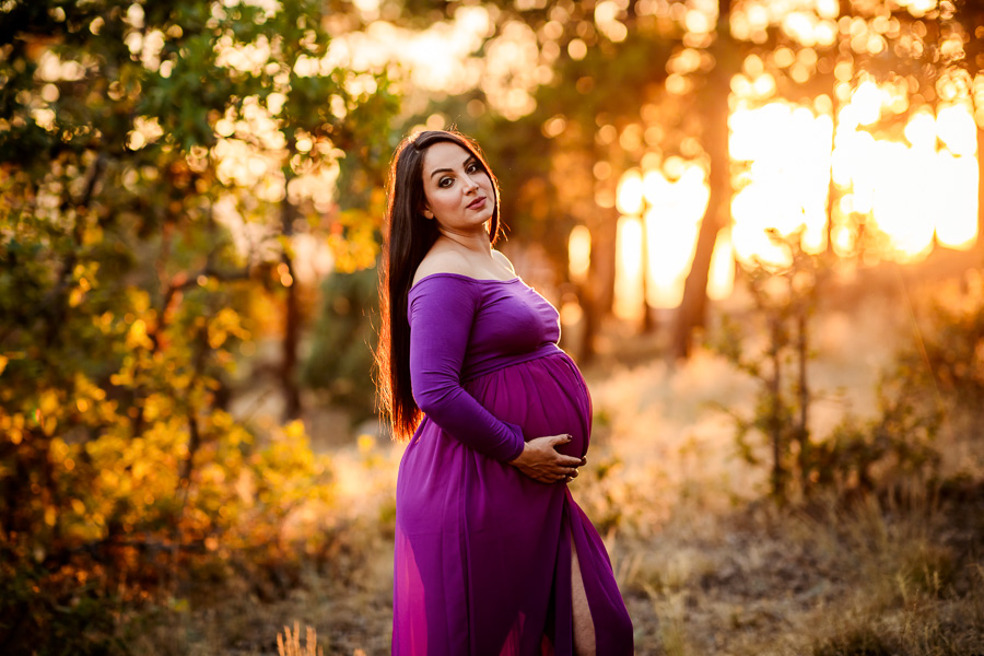 A woman in a flowy purple maternity dress in the woods