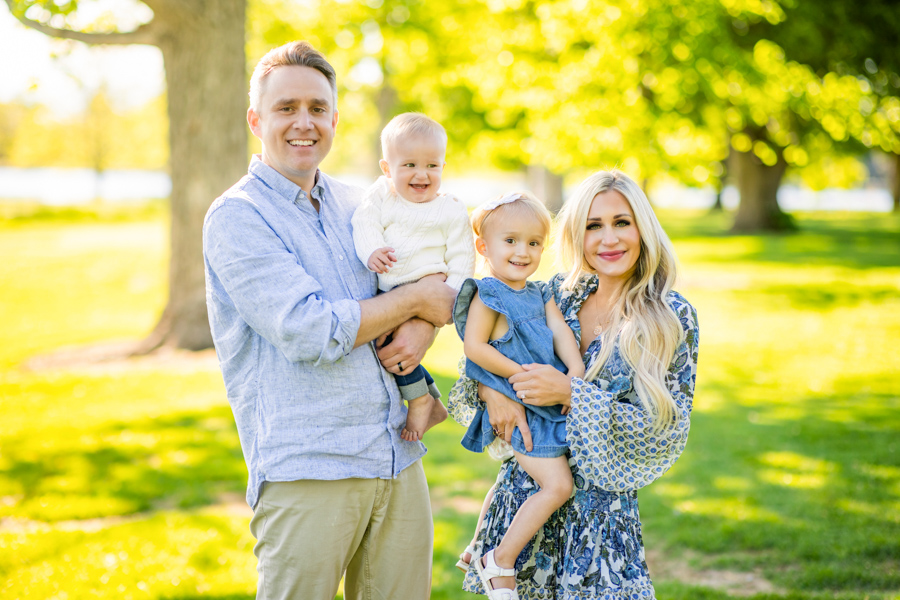 a mom and dad holding their kids at the park while wearing a blue and khaki palette