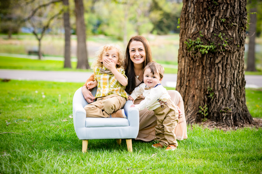 family of 3 wearing a brown and green color palette sitting on the grass on a spring day